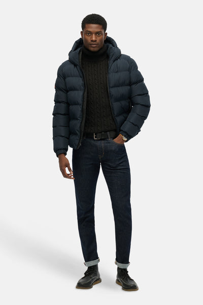 Veste courte bleue de SUPERDRY, portée avec un pull à col roulé en maille torsadée et un jean sombre.
