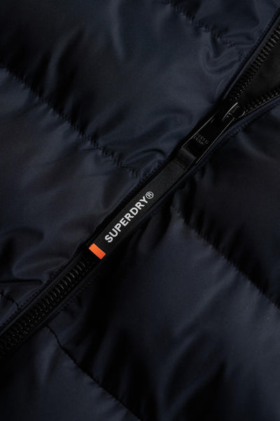Veste courte bleue de SUPERDRY, avec une fermeture éclair noire et le logo de la marque visible.