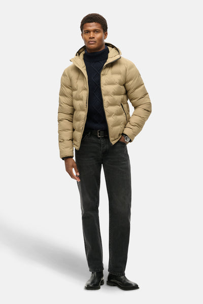 Veste de pluie beige de SUPERDRY, portée avec un pull en maille torsadée et un jean noir.