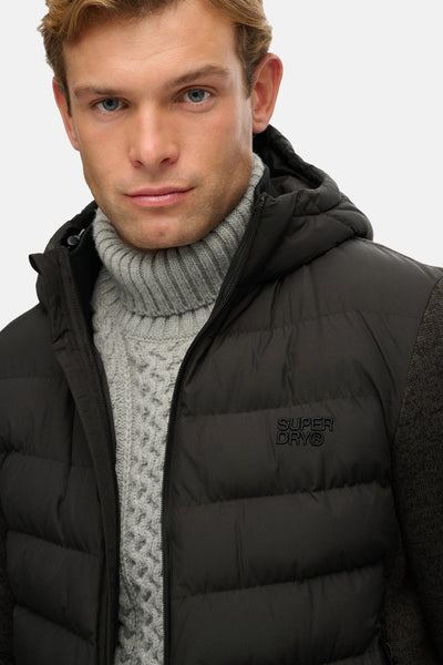 Imperméable noir de SUPERDRY avec capuche et fermeture éclair, porté avec un pull à col roulé gris.