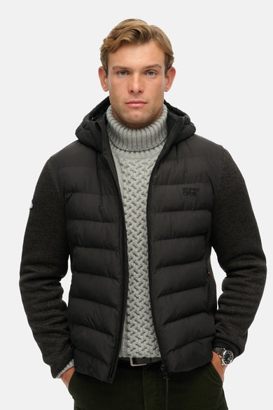 Veste de pluie noire de SUPERDRY avec capuche, manches en laine et un pull gris à col roulé en dessous.
