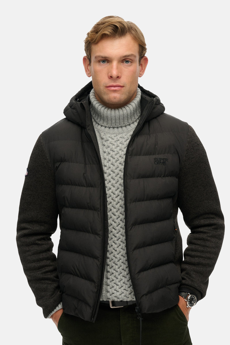 Veste de pluie noire de SUPERDRY avec capuche, manches en laine et un pull gris à col roulé en dessous.
