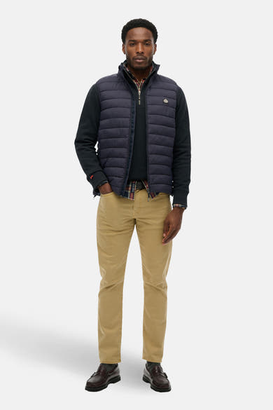 Blauwe bodywarmer van SUPERDRY, gedragen over een geruit overhemd en een beige chino broek.
