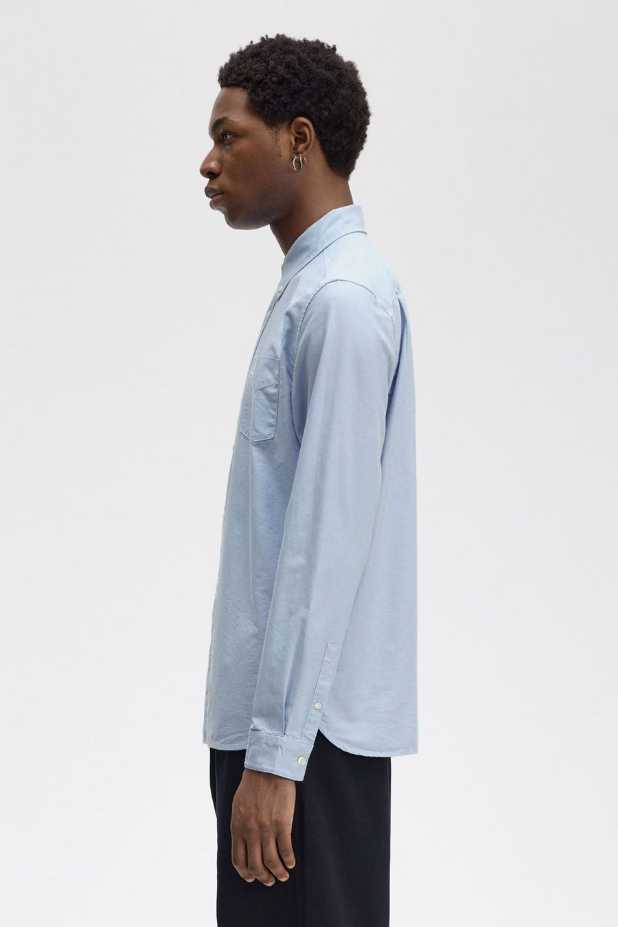 Blauwe blouse met lange mouwen van FRED PERRY, zijwaarts gezien, met borstzak en knopen bij de manchetten.