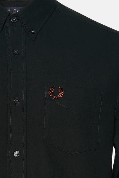 Gros plan sur une chemise verte à manches longues FRED PERRY, avec boutons et poche poitrine ornée d’un laurier brodé.