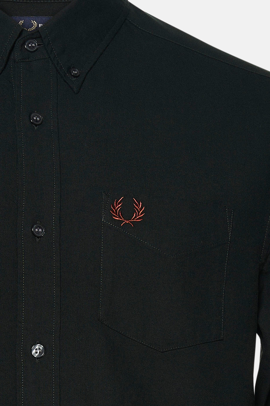 Gros plan sur une chemise verte à manches longues FRED PERRY, avec boutons et poche poitrine ornée d’un laurier brodé.