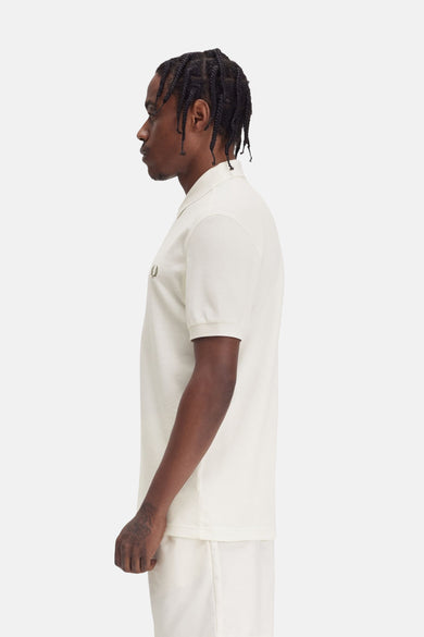 Polo à manches courtes écru de FRED PERRY, en maille piquée, vu de côté, porté avec un short blanc cassé.