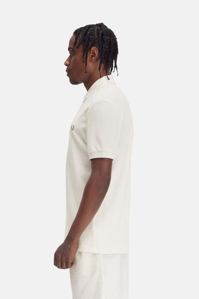 Polo à manches courtes écru de FRED PERRY, en maille piquée, vu de côté, porté avec un short blanc cassé.