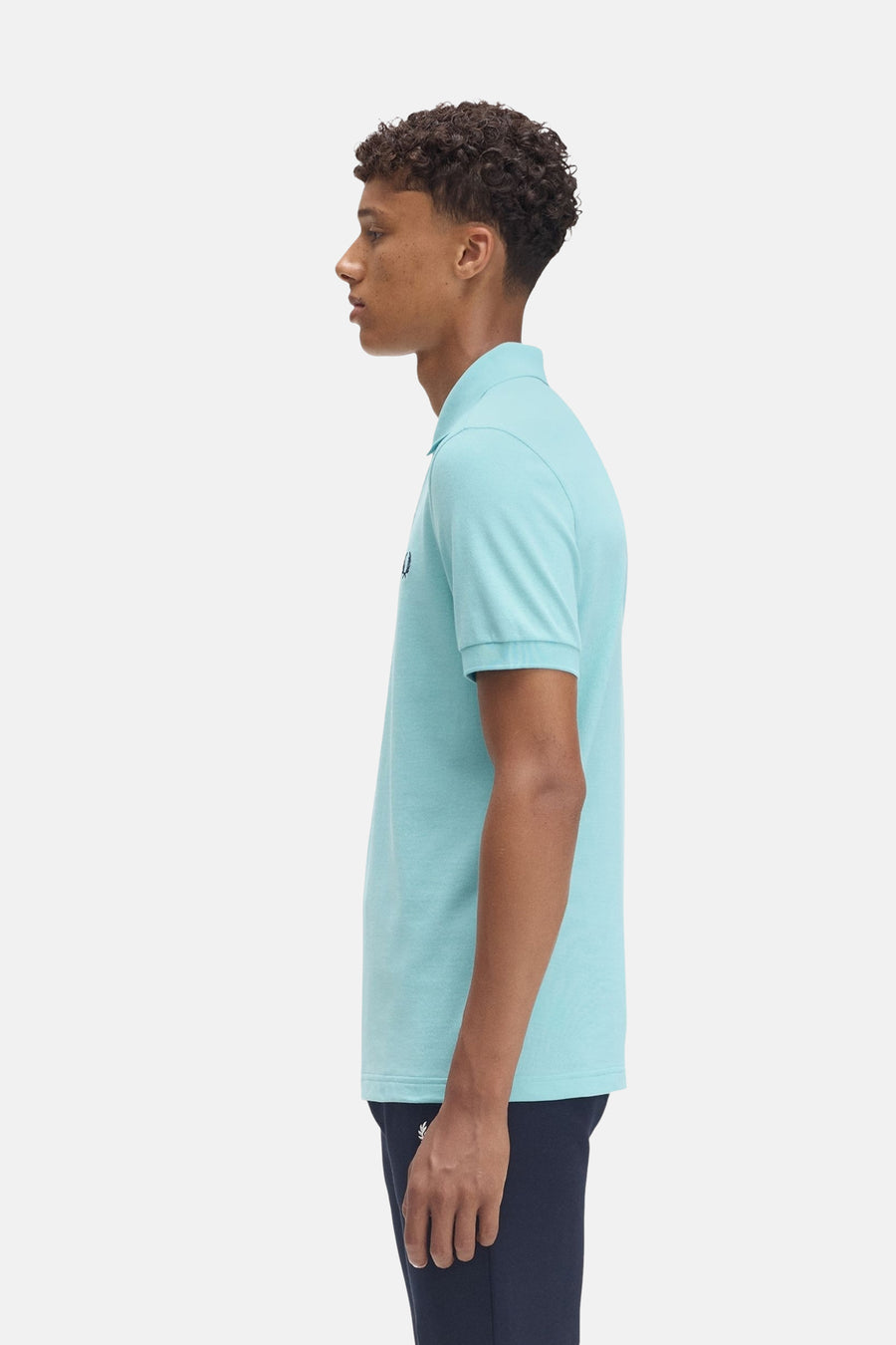 Turquoise poloshirt met korte mouwen van FRED PERRY, gedragen met een marineblauwe joggingbroek, zijaanzicht.