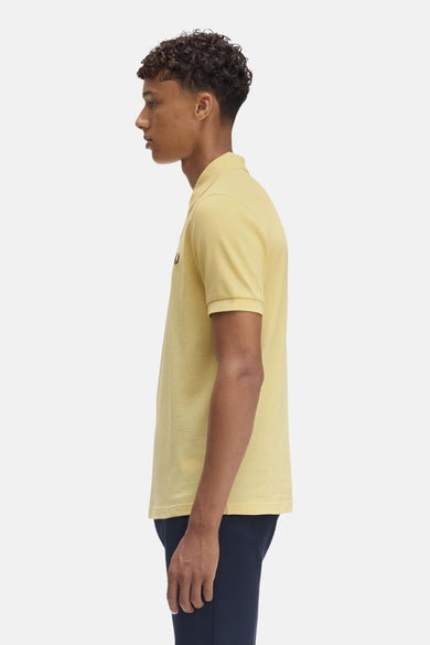 Gele poloshirt met korte mouwen van FRED PERRY, gedragen met een marineblauwe broek, zijwaarts gezien.