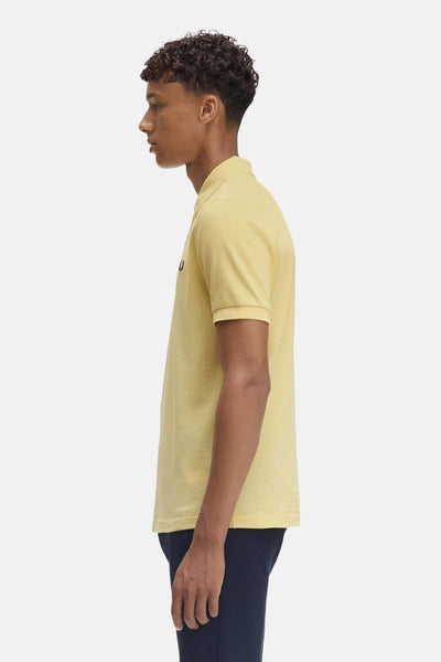 Gele poloshirt met korte mouwen van FRED PERRY, gedragen met een marineblauwe broek, zijwaarts gezien.