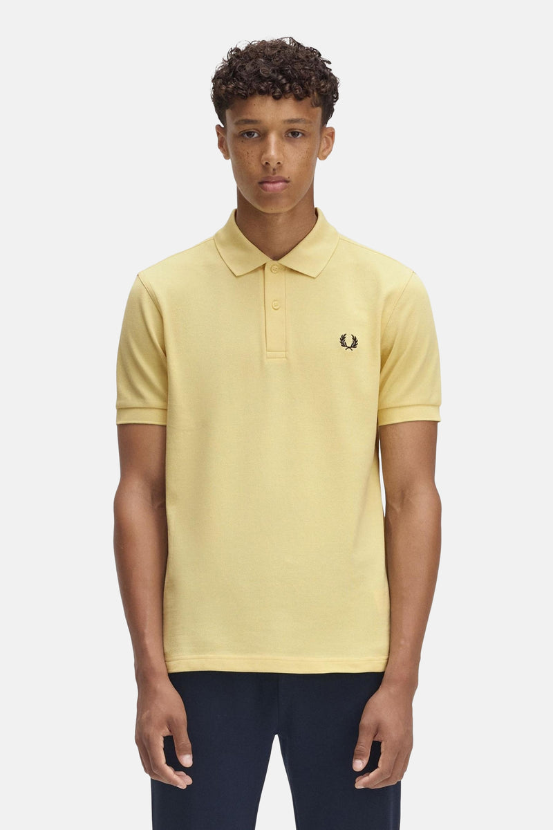 Gele Fred Perry poloshirt met korte mouwen, met geborduurd logo en gedragen met een marineblauwe broek.