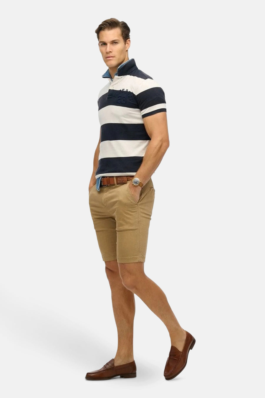 Short beige de SUPERDRY, porté avec une ceinture marron, une montre et des mocassins en cuir marron.