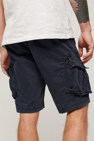 Short cargo bleu marine de SUPERDRY, porté avec un t-shirt blanc, poches cargo volumineuses et tatouage visible sur le bras.
