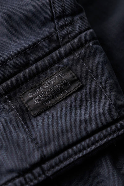 Korte blauwe SUPERDRY short, met zichtbaar geweven label en verstevigde naden, close-up.