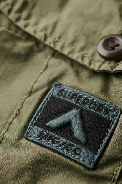 Short vert en coton de SUPERDRY, avec un patch décoratif brodé et un bouton marron visible.