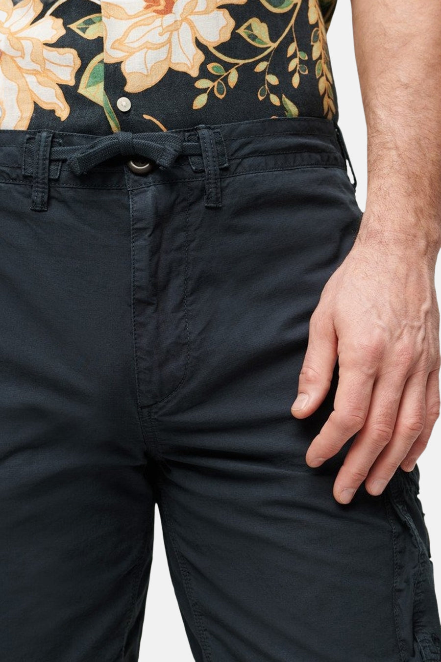 Korte blauwe SUPERDRY short, met trekkoord, gedragen met een bloemenhemd.