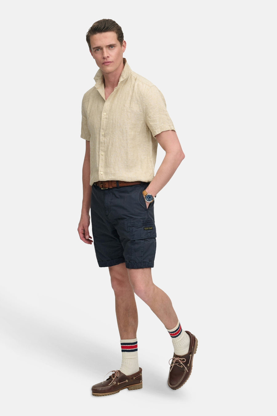 Kort marineblauw cargoshort van SUPERDRY met zijzakken en omgeslagen zomen, gedragen door een man in een overhemd.