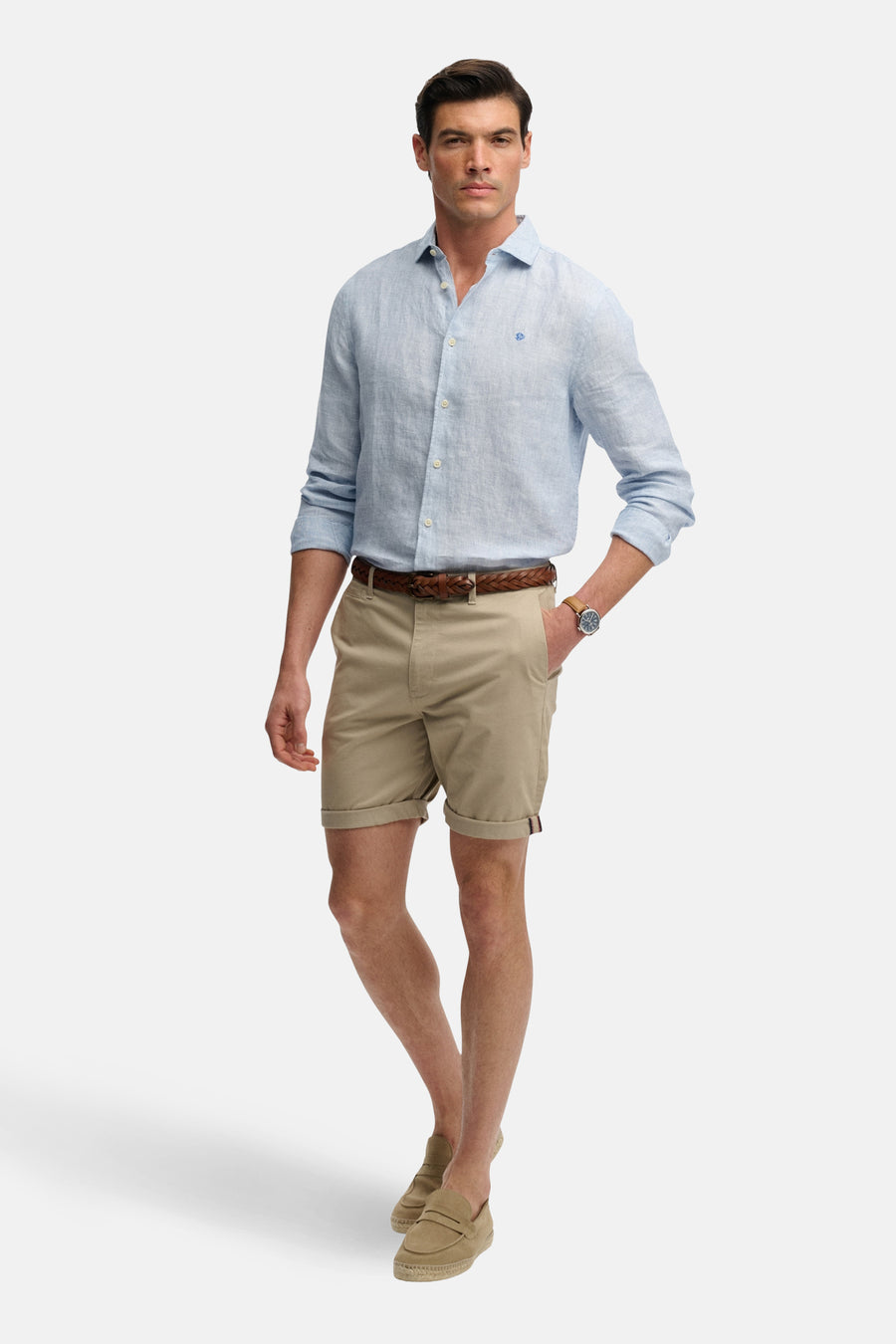 Korte beige short van SUPERDRY, gedragen met een gevlochten riem en een lichtblauw linnen overhemd, model met bootschoenen.