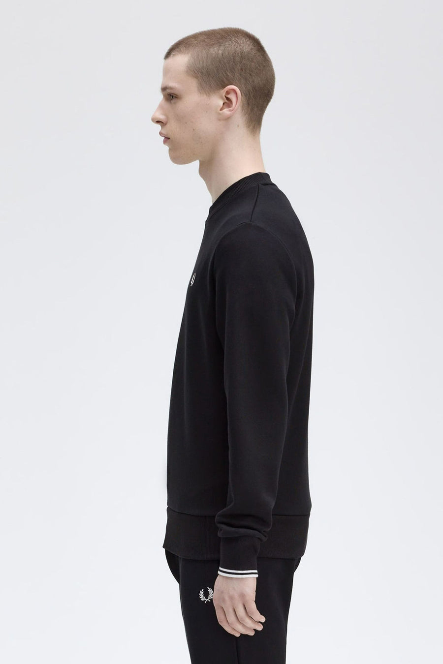 Zwarte rondehals sweatshirt van Fred Perry, met het logo op de voorkant, in profielaanzicht.
