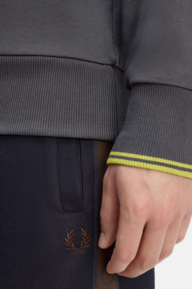 Sweat-shirt col rond gris de Fred Perry, avec des rayures jaunes à l'extrémité des manches et logo sur le pantalon.