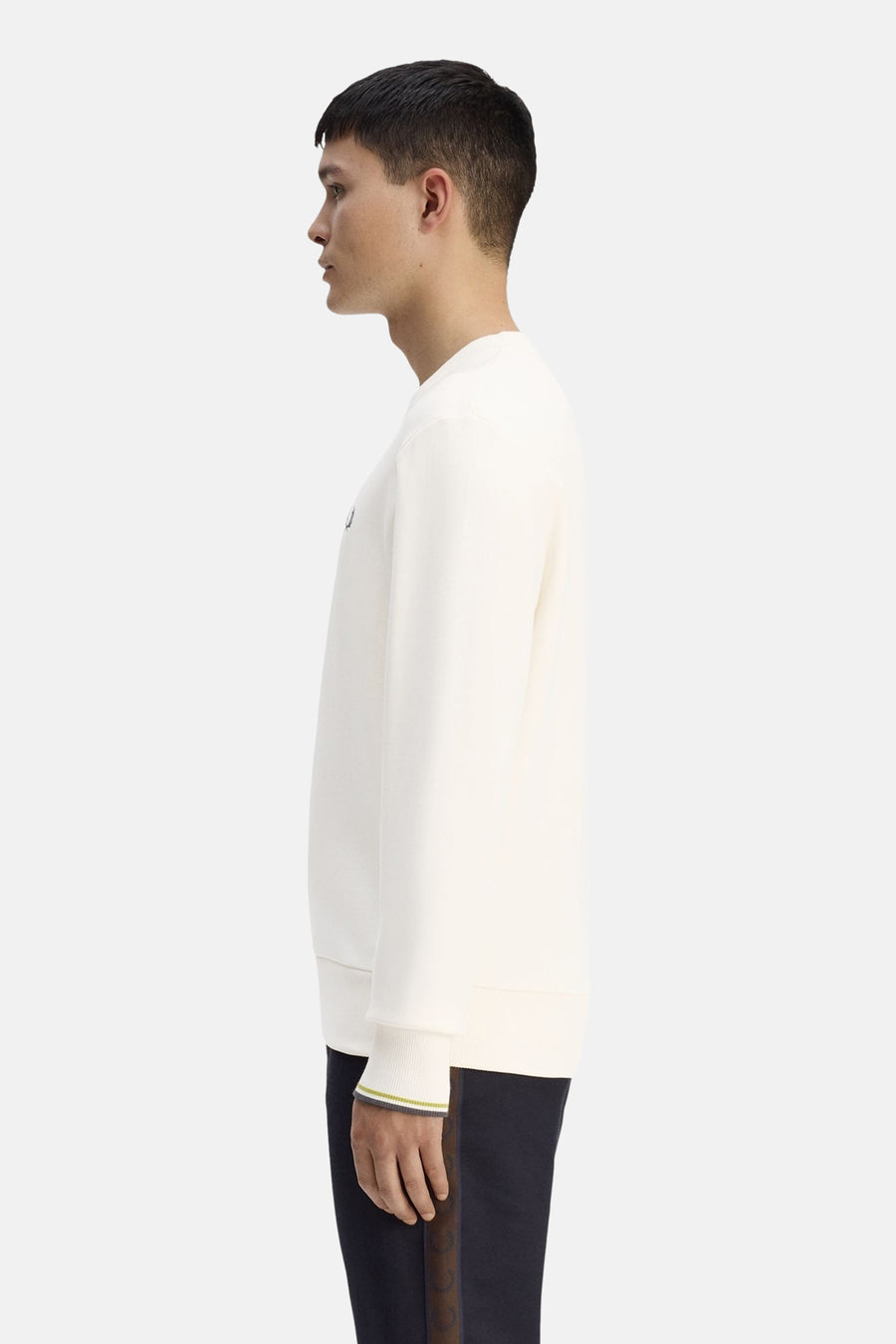 Ecru crewneck sweatshirt with ribbed cuffs and small chest logo, side view on model wearing dark pants