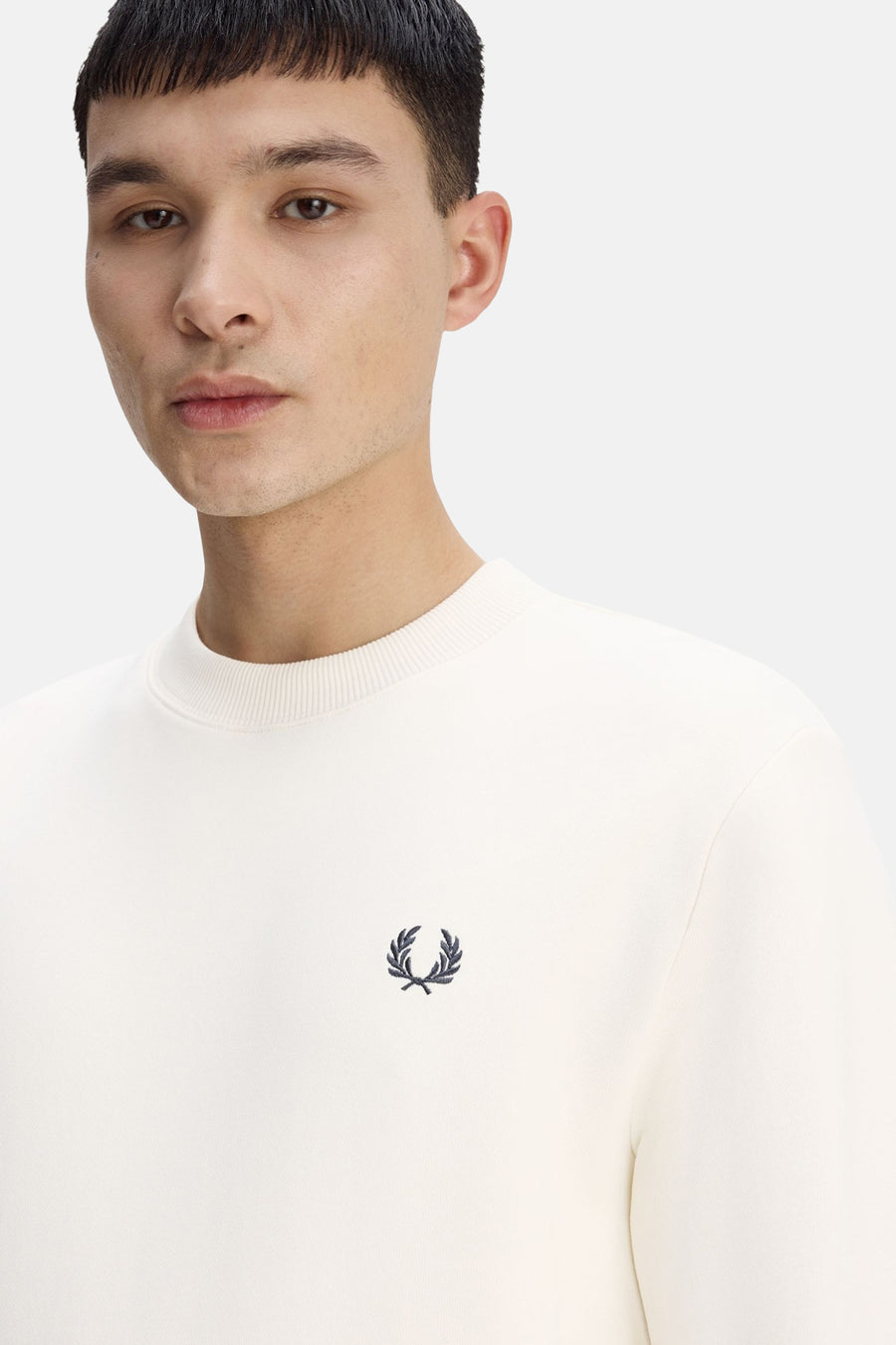 Ecru crewneck sweatshirt by Fred Perry with small black laurel wreath embroidery on chest, ribbed neckline, close-up front view
