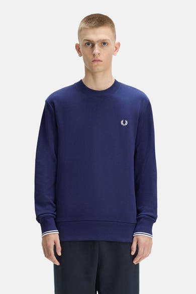 Blauwe rondehals sweatshirt van FRED PERRY met wit lauriertaklogo op de borst, gedragen door een man.