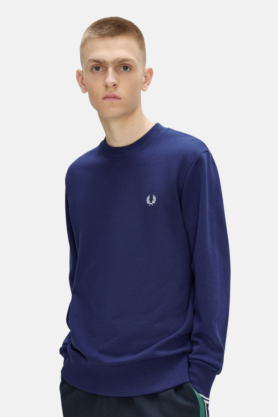 Sweat col rond bleu de FRED PERRY avec le logo couronne de laurier blanc sur la poitrine, porté par un homme.