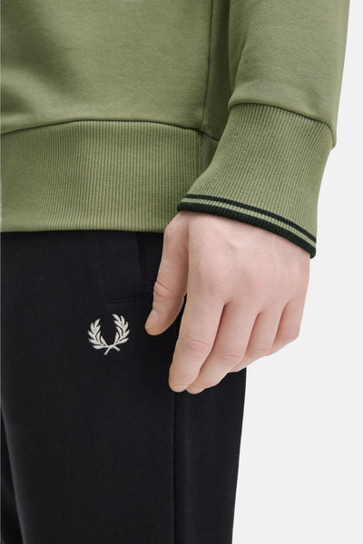 Sweat olive de Fred Perry, avec un logo brodé sur le pantalon noir.