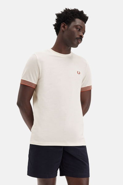 Ecru T-shirt met korte mouwen van Fred Perry met contrasterende strepen op de mouwen, gedragen met een marineblauwe short.