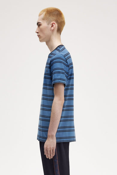T-shirt à manches courtes bleu FRED PERRY, à rayures horizontales noires, porté avec un pantalon de survêtement noir.