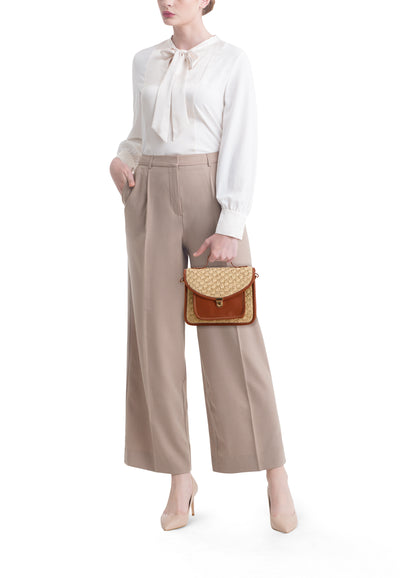 Cognac crossbody bag with woven texture and flap closure, held by model in beige pants and white blouse, front view