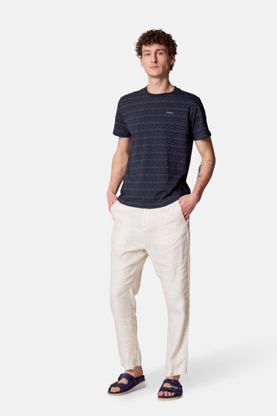 Pantalon de costume beige de Le Fabuleux Marcel de Bruxelles, porté avec un t-shirt rayé et des sandales bleues.
