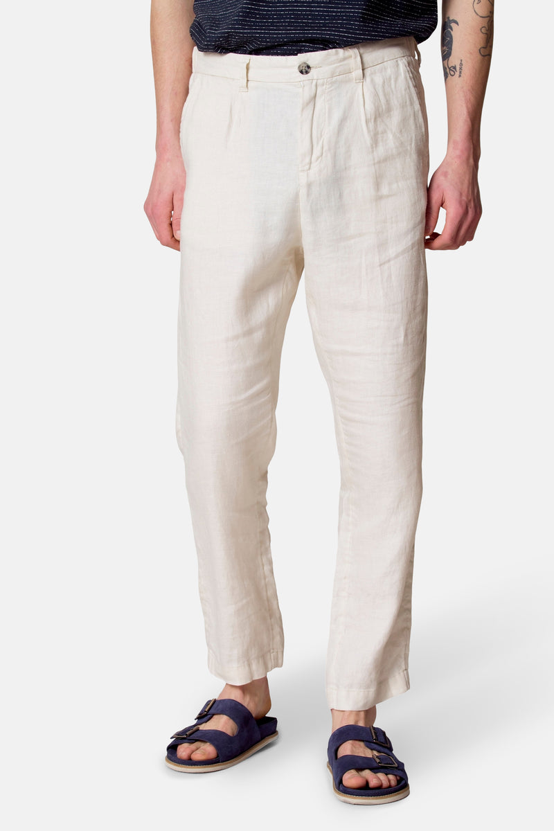 Pantalon de costume beige par Le Fabuleux Marcel de Bruxelles, en lin texturé, porté avec des sandales bleues.
