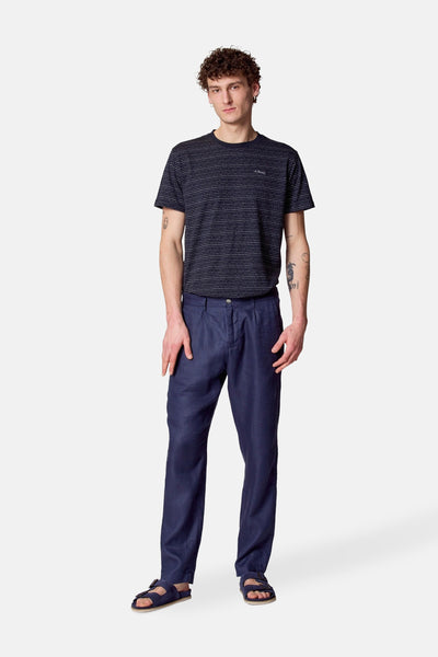 Pantalon de costume bleu par Le Fabuleux Marcel de Bruxelles, porté avec un t-shirt rayé et des sandales en cuir.
