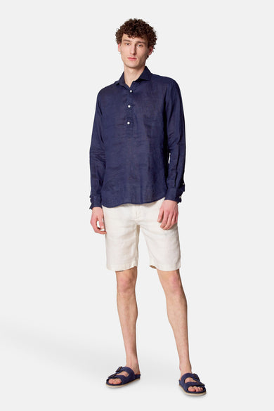 Short beige de Le Fabuleux Marcel de Bruxelles, porté avec une chemise bleu marine et des sandales bleues.