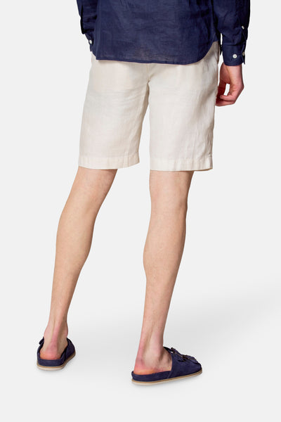 Korte beige short van Le Fabuleux Marcel de Bruxelles, gedragen met een blauw overhemd en suède muiltjes.