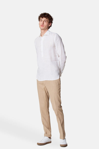 Chemise blanche à manches longues par Le Fabuleux Marcel de Bruxelles, portée avec un pantalon beige et des baskets blanches.