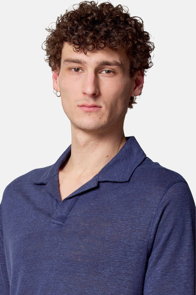 Polo bleu à manches courtes de Le Fabuleux Marcel de Bruxelles, porté par un homme avec des boucles et des boucles d'oreilles.