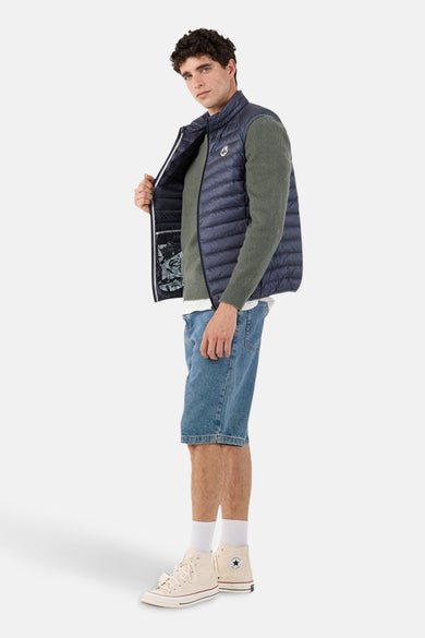 Blauwe mouwloze jas van JOTT, gedragen over een groene trui, met een spijkerbroekshort en hoge sneakers.