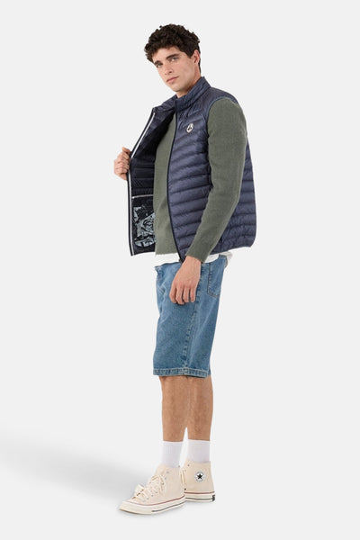 Blauwe mouwloze jas van JOTT, gedragen over een groene trui, met een spijkerbroekshort en hoge sneakers.