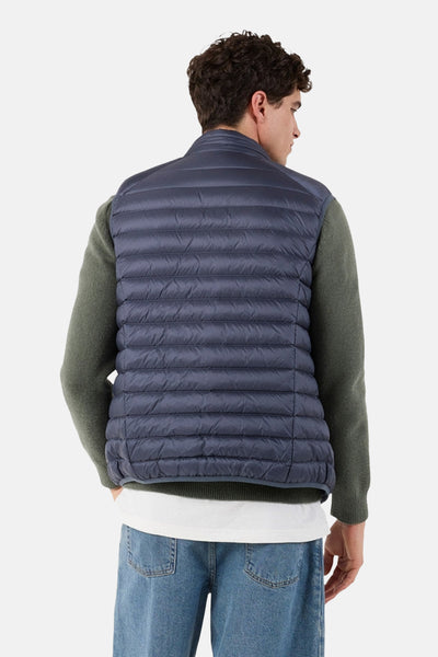 Blauwe mouwloze jas van JOTT, gedragen over een groene gebreide trui, met een lichtblauwe jeans.