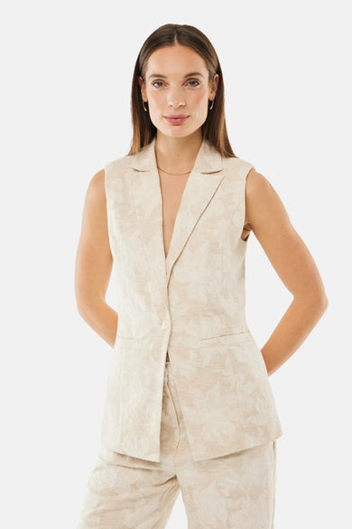 Blazer beige à motif floral by MEXX, coupe sans manches, porté avec un pantalon assorti.