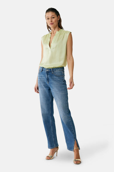 Blouse vert clair sans manches de MEXX, portée avec un jean bleu et des sandales dorées.
