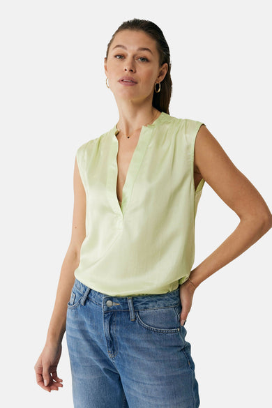 Chemisier vert sans manches de MEXX, avec un col en V et porté avec un jean bleu.
