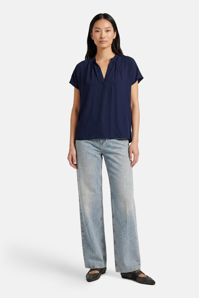 Blouse bleue à manches courtes de MEXX, portée avec un jean ample et des ballerines cloutées.
