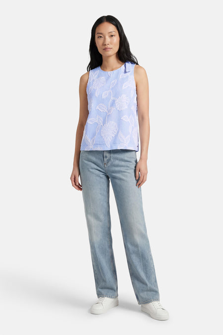 Chemisier sans manches bleu rayé de MEXX, avec motif floral blanc en relief et col rond. Porté avec un jean bleu et des baskets blanches.
