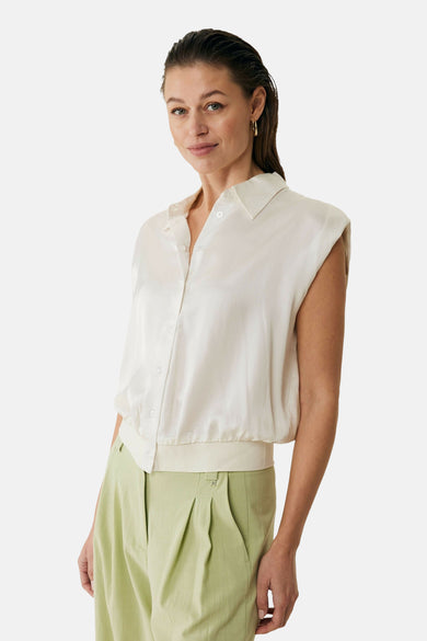 Ecru mouwloos blouse van MEXX, met kraag en plooien aan de achterkant, gedragen met een groene broek.