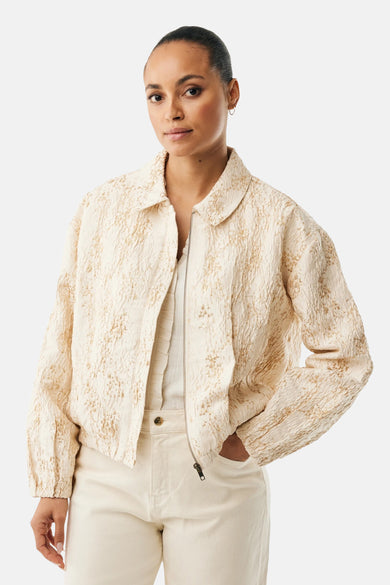 Veste courte beige de MEXX, à texture travaillée, portée sur un haut uni et un pantalon coordonné.
